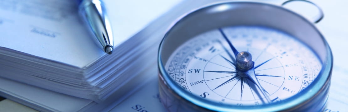 A close-up of a compass and pen resting on a stack of documents.